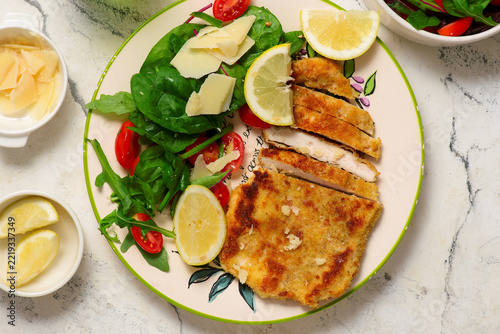 Chicken Milanese with lemon wedges and a salad of arugula, cherry tomatoes, and Parmesan