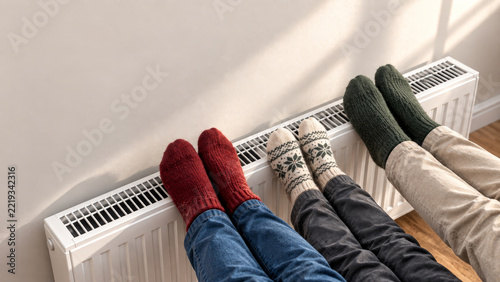 Family in warm socks by radiator, heating home in cold winter and autumn, energy savings during seasonal heating period.