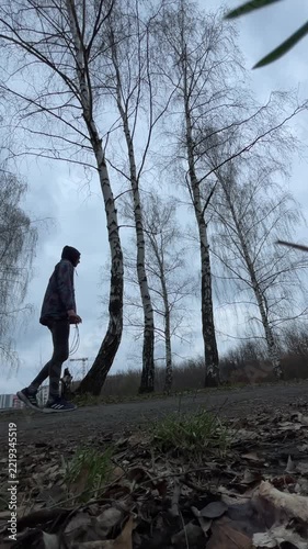Black man vertical final jump finish park, hoodie stopping under birch trees with breath and relief, lowangle vertical frame capturing end of workout and quiet completion