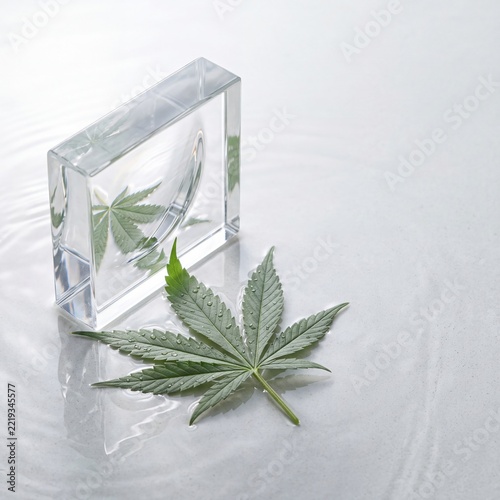 Cannabis leaf and glass cube on reflective surface