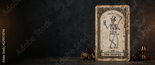 Vintage tarot card depicting a skeleton reaper with scythe and goblet on dark tabletop. Death tarot symbolism and gothic Halloween. Occult divination, spooky vintage decor. Copy space banner