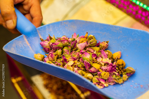 Vibrant dried flower petals in a tray being scooped by a hand