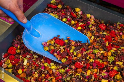 Vibrant dried flower petals in a tray being scooped by a hand