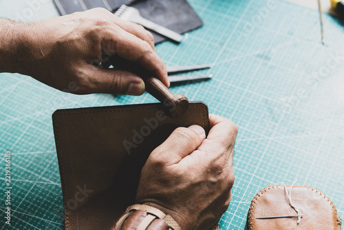 An artisan polishing the edges of a leather wallet with a wooden tool.