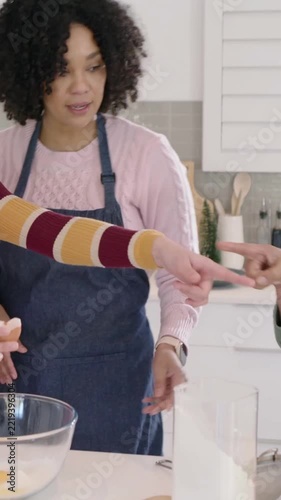 Vertical video: Cracking teen in red apron adding egg to bowl, adult in apron guiding batter mixing