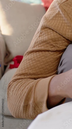 Vertical video: Adjusting arm, adult in tan sleeve reaching offscreen on couch with red pillow