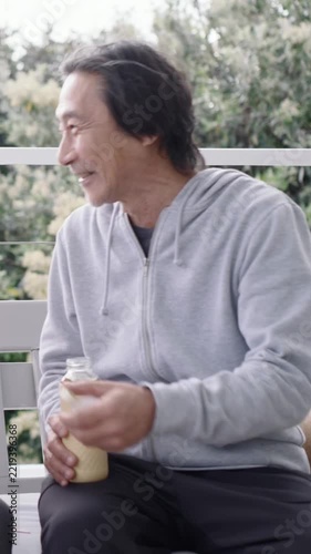 Vertical video: Hearing offscreen call, Japanese senior turning on porch, offering cap, copy space