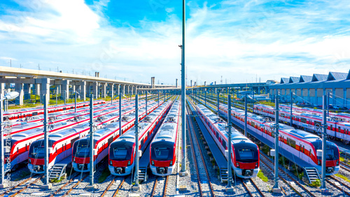 Rows of modern commuter trains parked at a railway maintenance depot. Aerial view of multiple red and white passenger trains at a service station. High angle view of metropolitan transit trains.