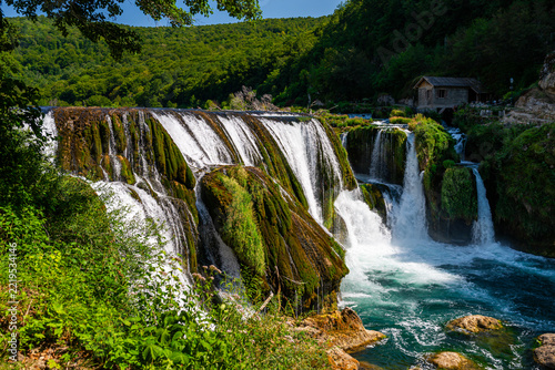 Wide moss-covered Strbacki Buk waterfall with traditional watermill, Una River, Bosnia