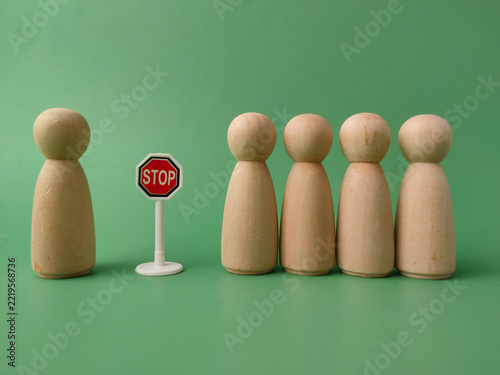 A line of wooden peg dolls faces a single doll standing opposite a miniature stop sign