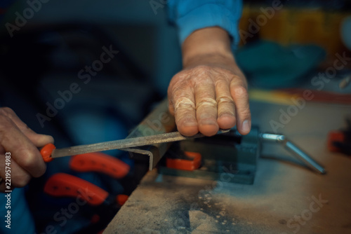Close-up of skilled hands using a metal file to shape and smooth a metal piece clamped in a vise. Authentic metalworking photo for industrial, craft and maker projects