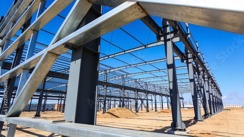 Large Industrial Steel Building Framework Under Construction with Galvanized Columns and Roof Trusses Against Clear Blue Sky