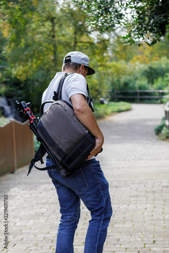 Male Photographer Carrying Camera Bag and Tripod While Walking in Green Park