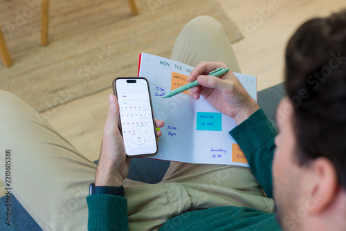 White person scheduling appointments in weekly planner with smartphone