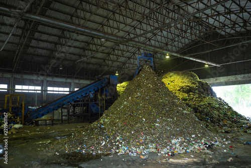 Heavy excavator loading piles of municipal solid waste onto an industrial trommel screen conveyor system inside