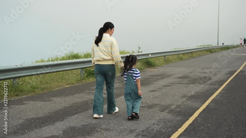 mother and preschool child girl holding hand and walking on a road on mountain in the morning