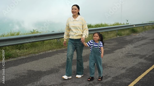 mother and preschool child girl holding hand and walking on a road on mountain in the morning