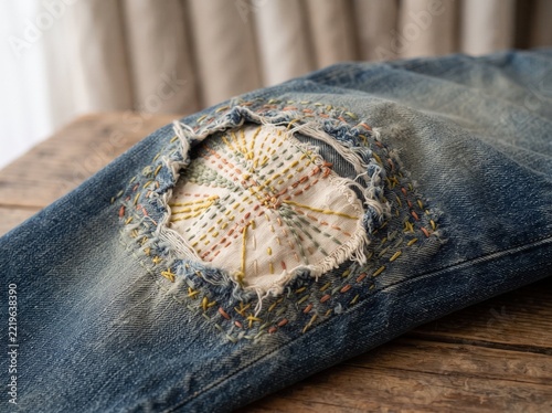 Visible Mending of Torn Blue Denim Jeans with Decorative Hand Stitching
