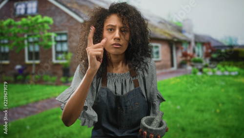Woman holding a mortar and pestle and pointing finger in front of a building; home cooking concentration.
