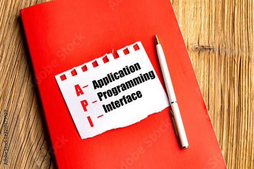Application programming interface text on torn paper with a red notebook and pen on a wooden desk