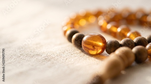 Close up of traditional amber and dark wooden prayer beads resting on a textured surface in soft warm light