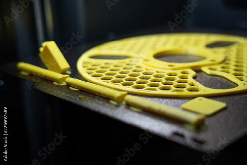 Yellow 3D printed plastic spool parts with honeycomb pattern resting on a textured build plate inside a printer chamber.