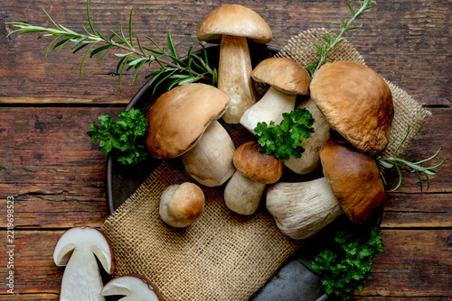 Fresh forest mushrooms, Boletus edulis (king bolete),  penny bun, cep, porcini, mushroom in an old bowl, plate and rosemary parsley herbs on the wooden dark brown table, top view background