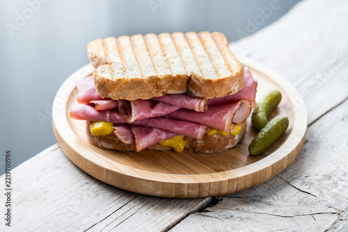 Grilled pastrami sandwich with mustard and pickles on rustic wooden table
