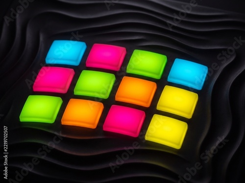 A grid of brightly lit, square buttons in neon colors like cyan, magenta, lime green, orange, and yellow are arranged on a dark, undulating background. 