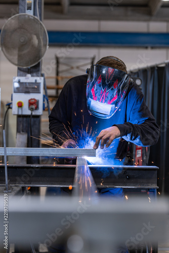 Welder in helmet welding a steel beam with bright blue arc and sparks