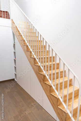 Fotografie Long wooden staircase with white balusters above white storage cabinets