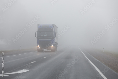 Truck on a country road in the thick fog. Poor visibility conditions on the road.