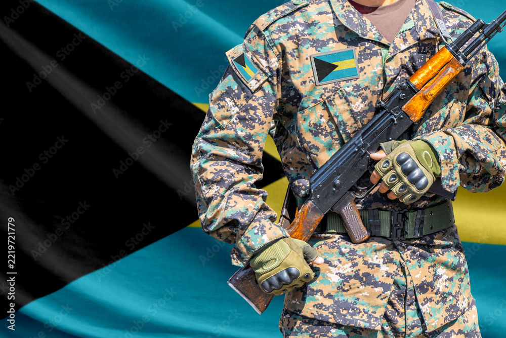 Fototapeta premium Bahamas flag with soldier in military uniform holding assault rifle in front of it