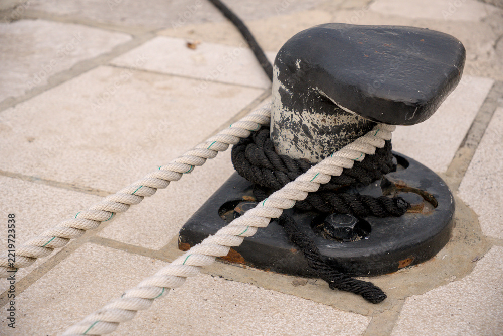 Fototapeta premium Cast iron mooring bollard with ropes on stone pier in morning harbor.