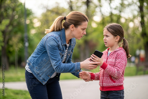Mother disciplining daughter about phone addiction in park