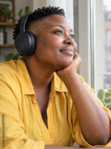 Woman listening to music in plain black headphones beside a bright window