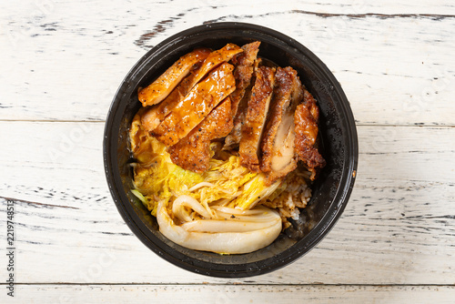Grilled chicken rice bowl with napa cabbage served in black plastic takeaway container
