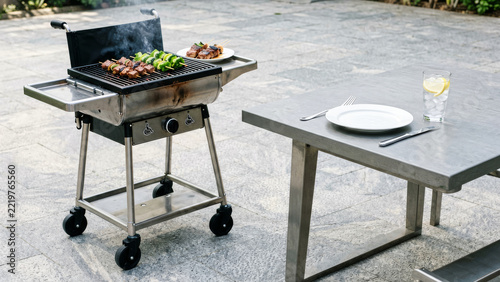 Charcoal barbecue grill beside an outdoor picnic table holds freshly cooked food on a sunny lawn creating an inviting weekend meal setting for backyard gatherings