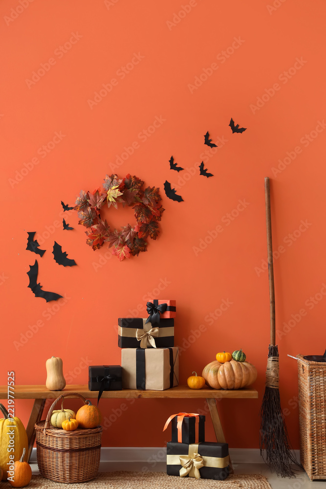 Fototapeta premium Halloween celebration and autumn holiday decor, festive gift boxes with pumpkins and fall wreath on wooden bench against orange wall with paper bats