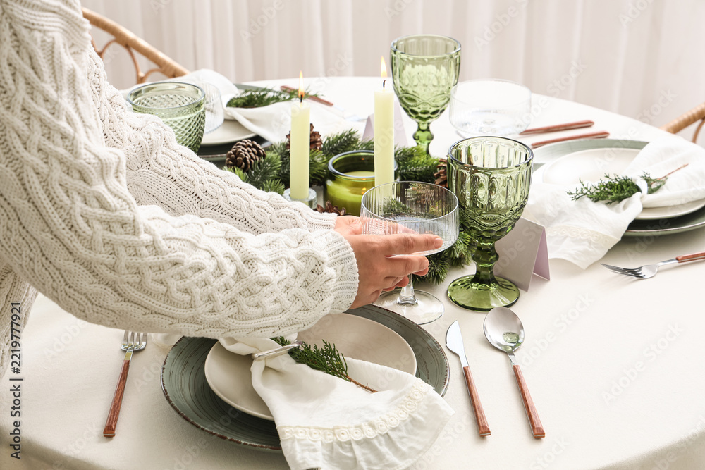 Fototapeta premium Christmas dinner preparation, woman setting festive table with green glassware and candles for holiday celebration and winter home hospitality