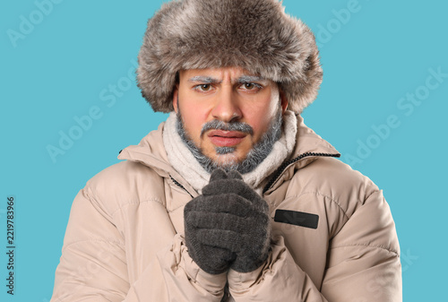 Young man in warm gloves, winter clothes and with frosted beard shivering fro...