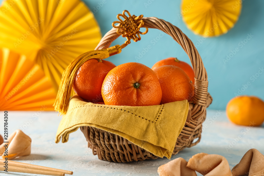 Fototapeta premium Lunar New Year celebration, fresh mandarin oranges in a wicker basket with traditional gold tassel and paper fans for prosperity and good fortune