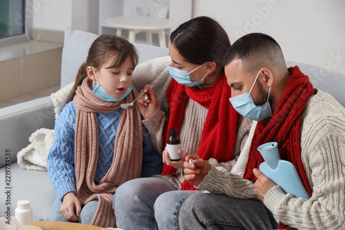 Ill family in medical masks taking cough syrup on sofa at home