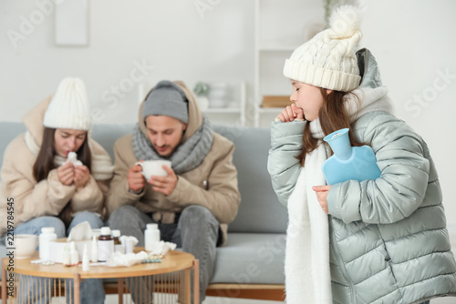 Ill girl in winter clothes with hot water bottle and her parents at home