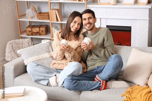 Loving couple holding cups of cocoa with marshmallows at home on winter day