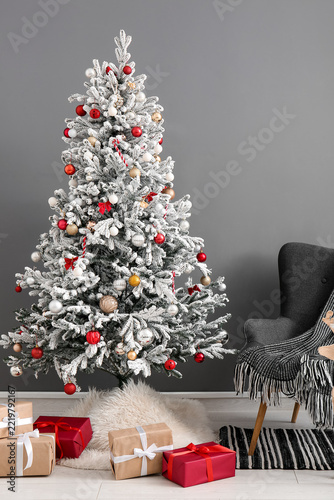 Beautiful Christmas tree with gift boxes and comfortable armchair near grey wall