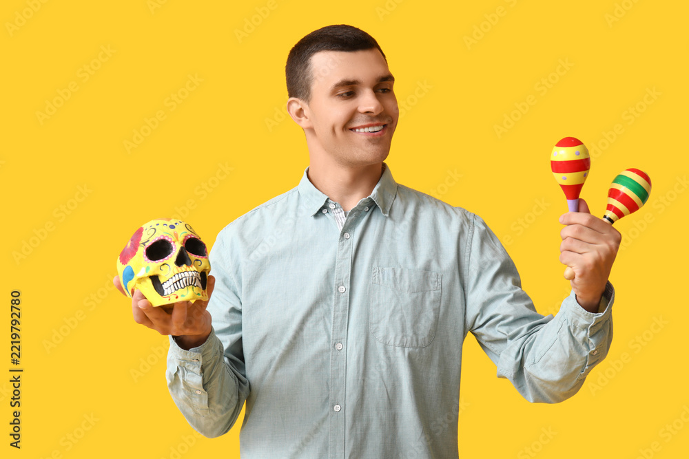 Fototapeta premium Dia de los muertos celebration, man holding traditional sugar skull and maracas for mexican holiday festival and cultural heritage event on yellow background