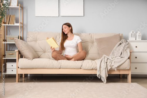 Mindfulness and relaxation, pregnant woman reading a book on a sofa at home f...