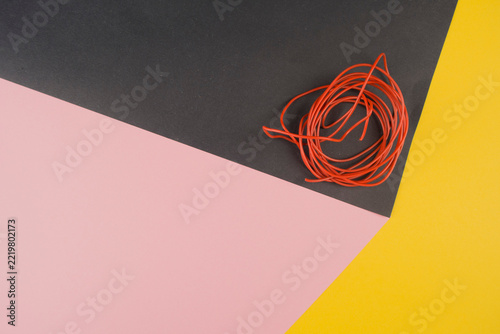 a tangled bundle of bright red cord lies on a pastel pink, gray, and yellow background, creating a minimalist abstract composition