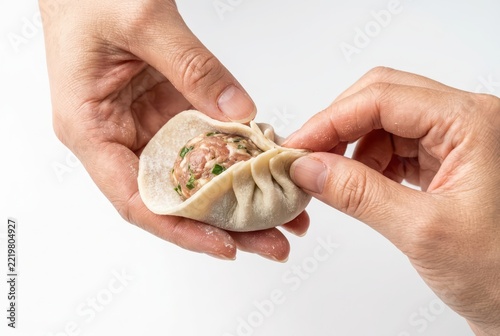 Close-up of Hands Making Traditional Chinese Dumplings or Gyoza with Meat Filling on White Background